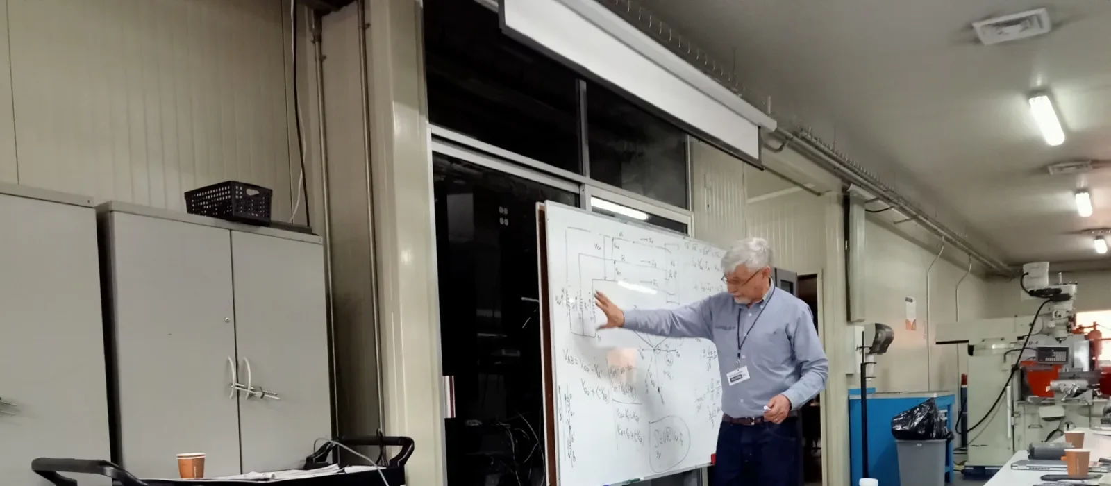Instructor explicando cálculo de potencia trifásica en pizarrón durante capacitación en taller